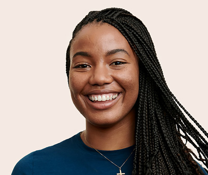 Apple Retail employee with long hair and a necklace, smiling at the camera.