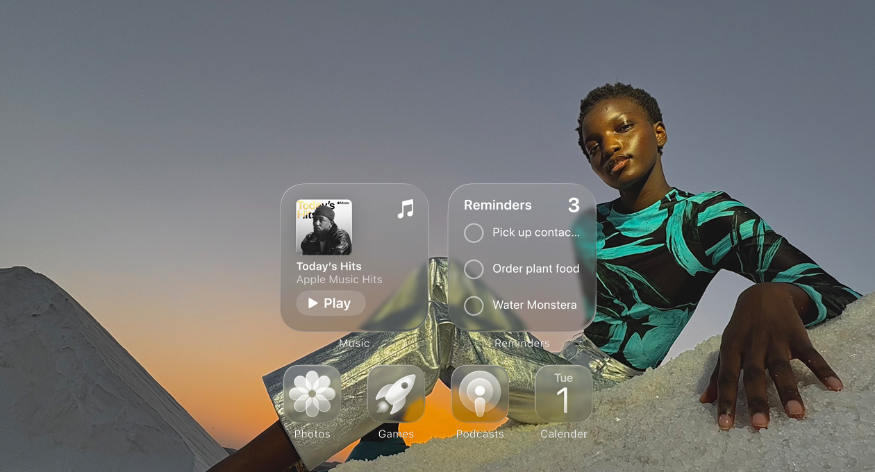 Displej v Liquid Glass designu s průsvitnými ikonami aplikací jako Apple Music, Připomínky, Fotky, Hry, Podcasty a Kalendář, přes které prosvítá tapeta