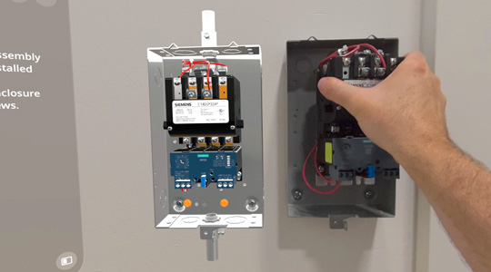 Une main installe un boîtier mécanique avec des fils sur un mur, près d’une projection 3D du même appareil