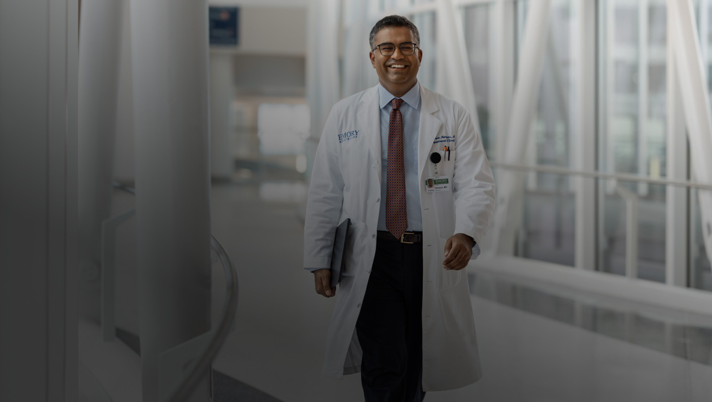 Médico segurando um MacBook embaixo do braço direito enquanto caminha.